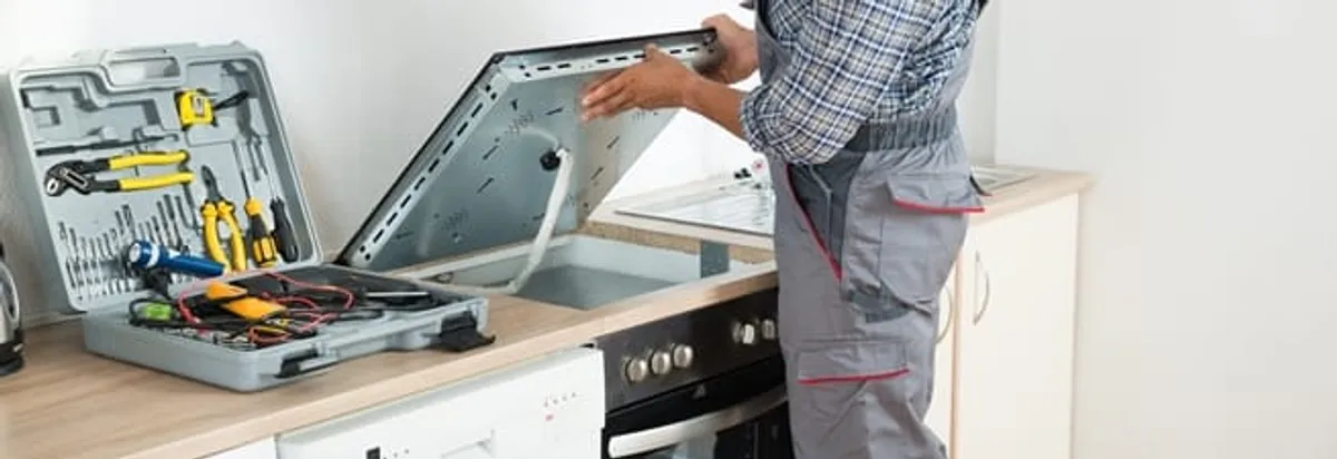 Cooktop repair technician lifting a built-in stovetop for service in Sacramento, CA