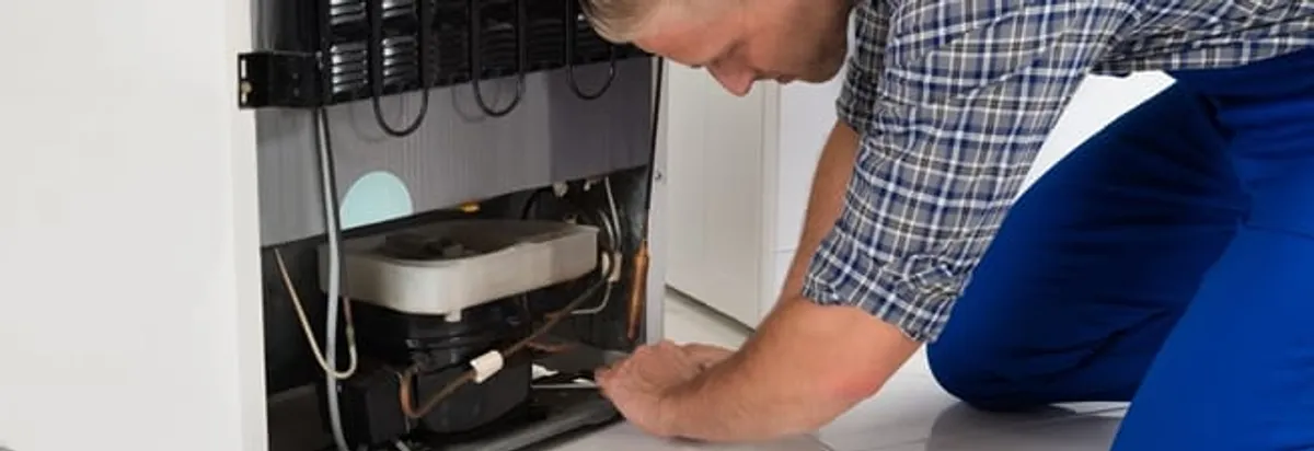 Refrigerator repair technician servicing the compressor and condenser area in Sacramento, CA